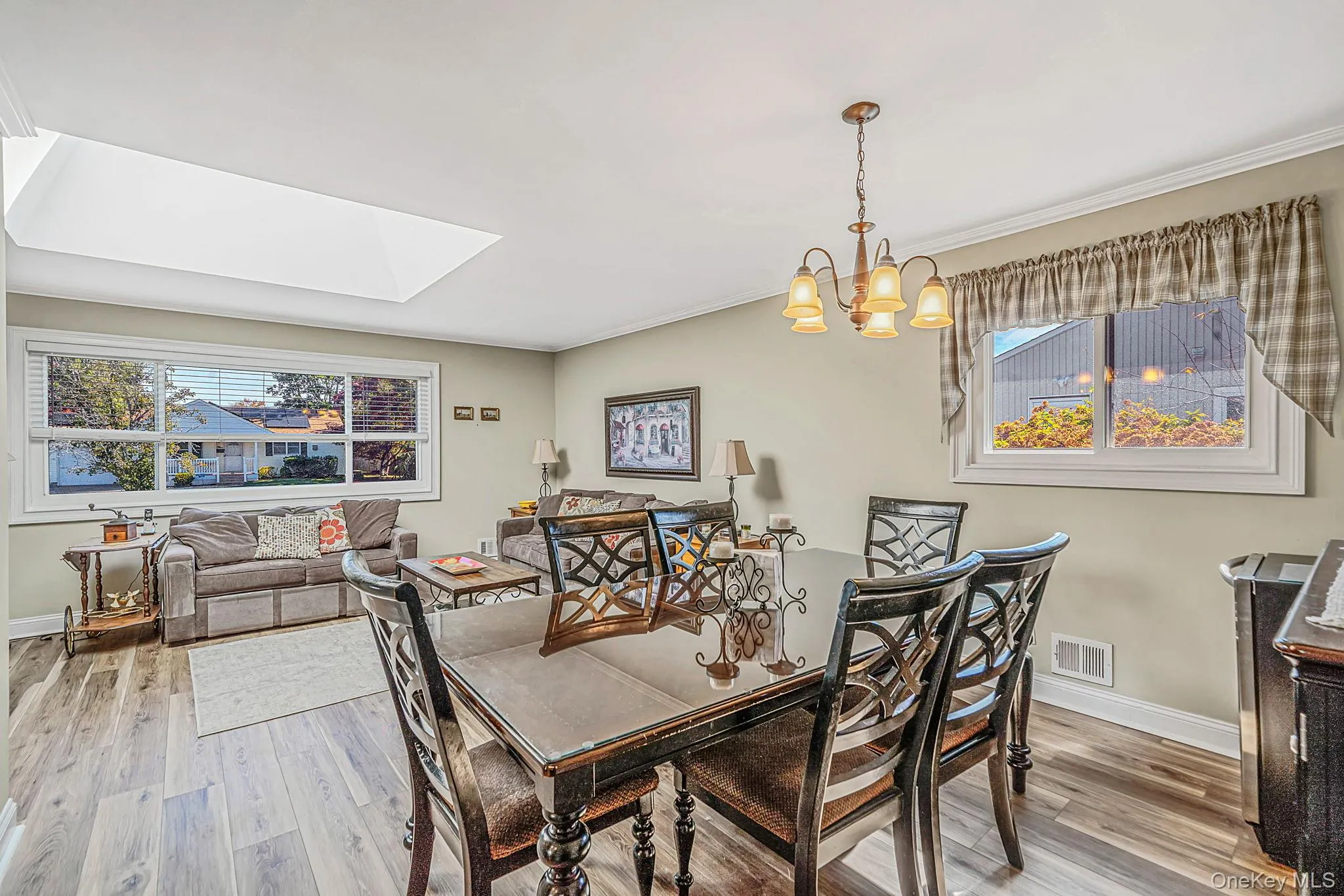 Living area featuring wood-finish flooring, a large ceiling skylight, oversized windows, and a multi-arm chandelier Living area featuring wood-finish flooring, a large ceiling skylight, oversized windows, and a multi-arm chandelier