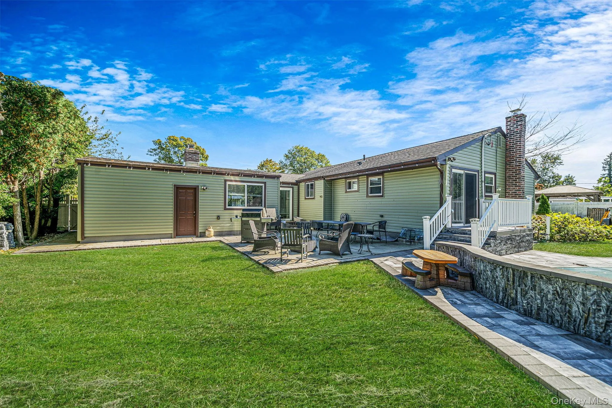 Exterior featuring horizontal siding, a multi-level stone retaining wall, a paved patio, and a staircase with white railings Exterior featuring horizontal siding, a multi-level stone retaining wall, a paved patio, and a staircase with white railings