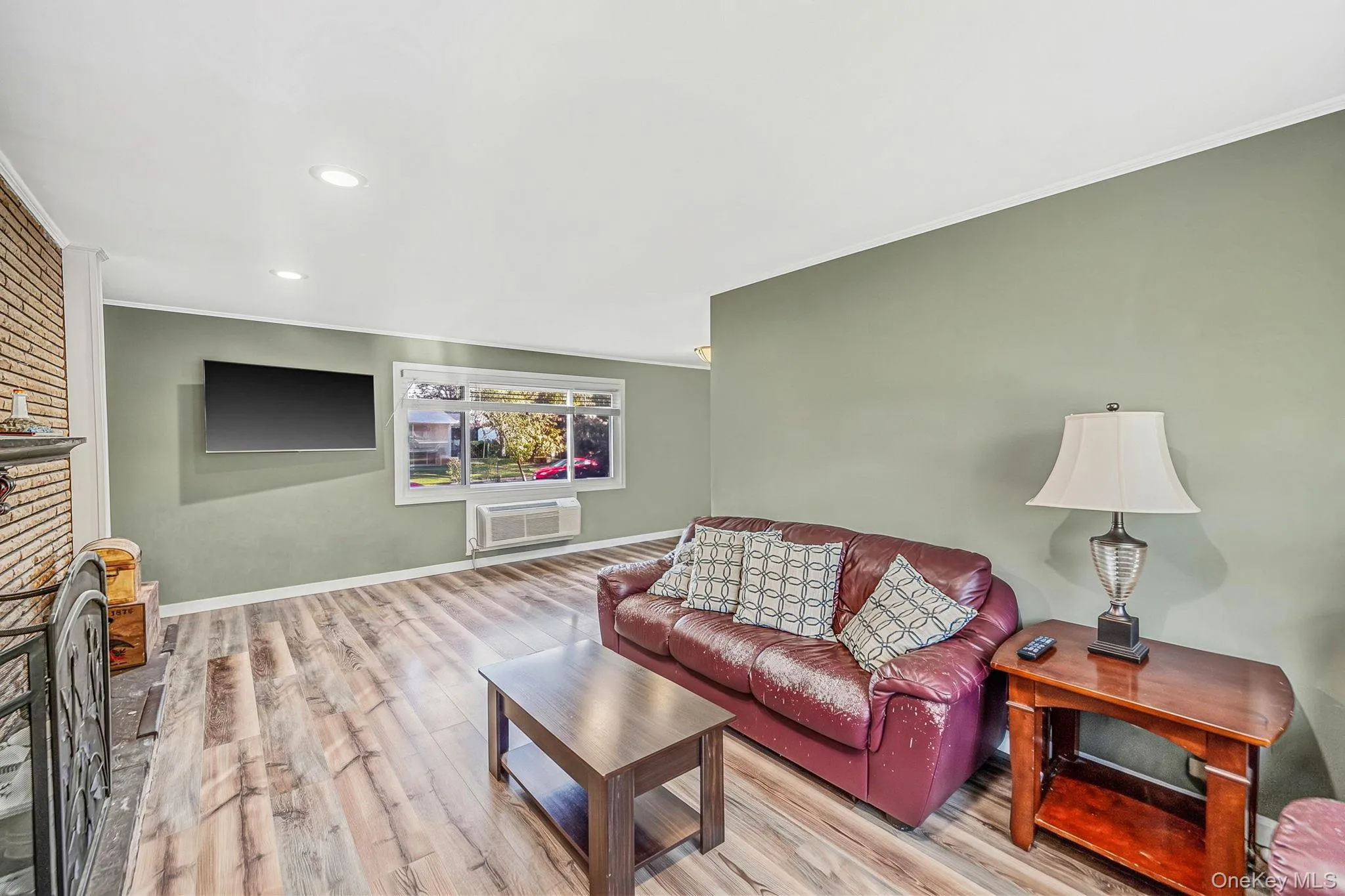 Living area featuring wood-finish flooring, recessed lighting, and a floor-to-ceiling brick fireplace surround Living area featuring wood-finish flooring, recessed lighting, and a floor-to-ceiling brick fireplace surround