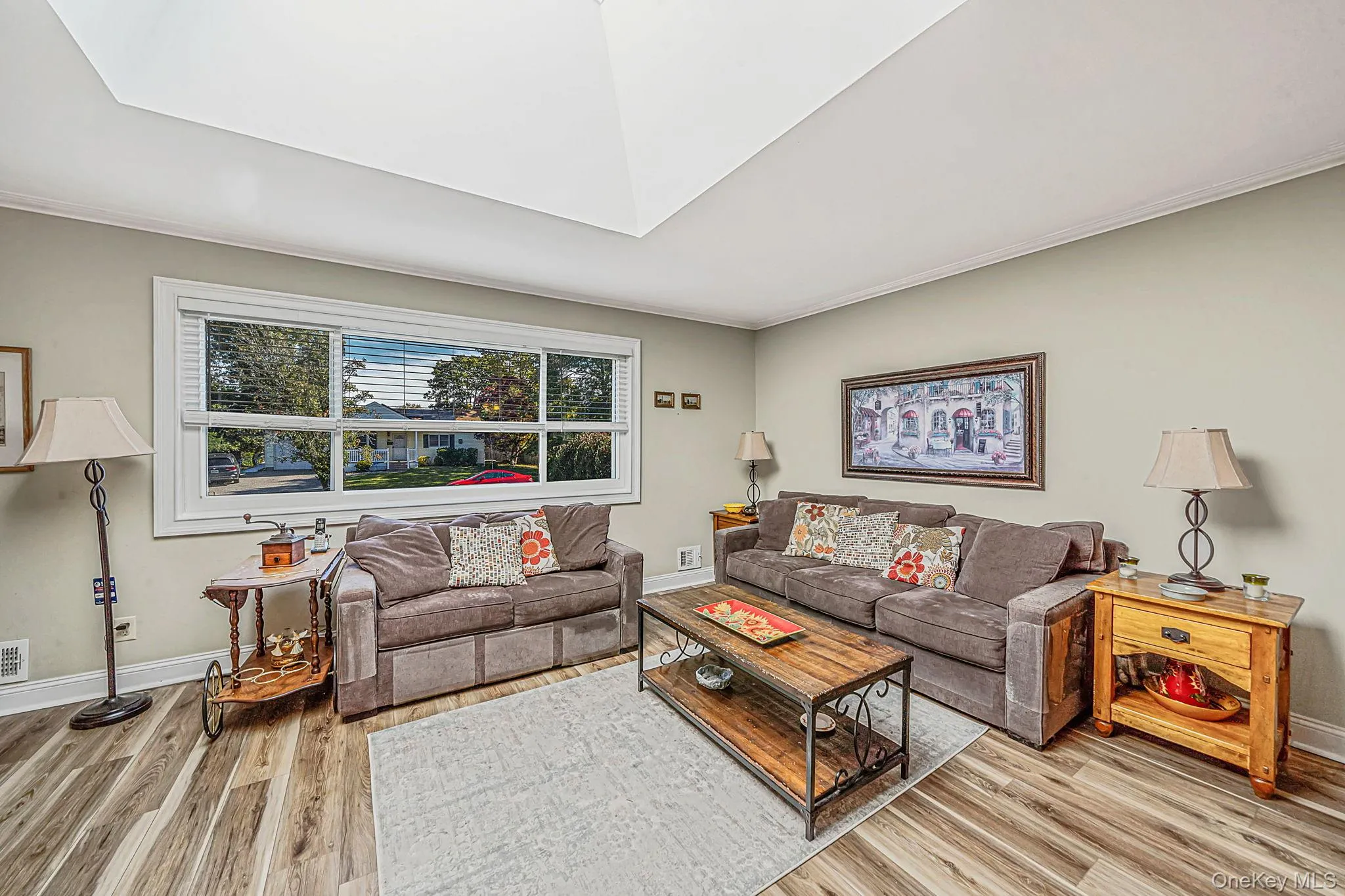 Living area featuring a vaulted ceiling with skylight, wood-finish flooring, and a large horizontal window Living area featuring a vaulted ceiling with skylight, wood-finish flooring, and a large horizontal window