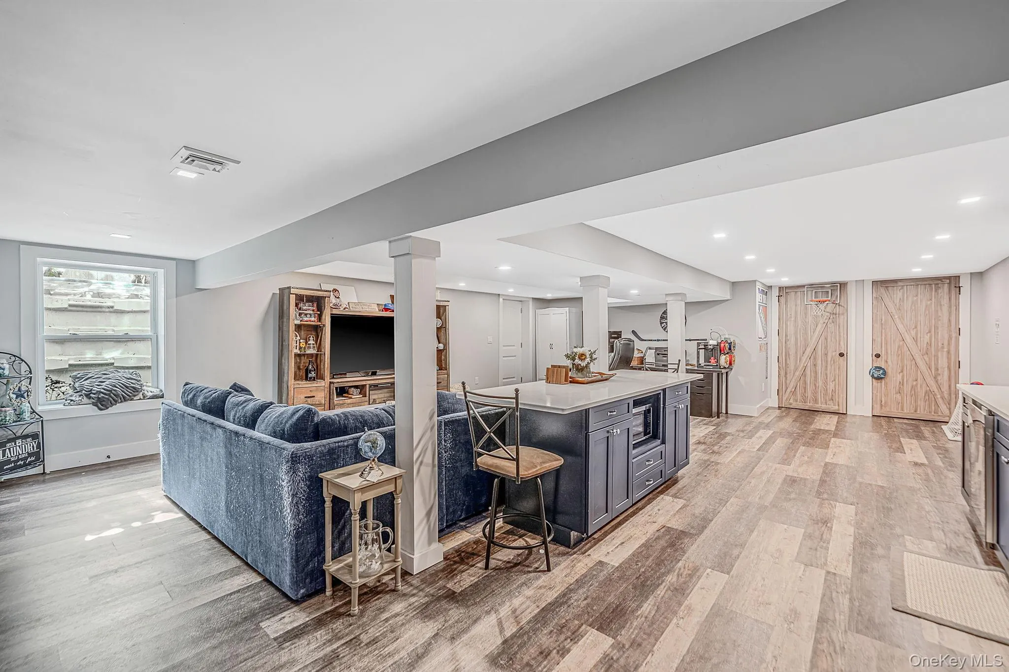 Open-concept area featuring wood-finish flooring, recessed lighting, a central island with a stone countertop, and custom barn-style wooden doors Open-concept area featuring wood-finish flooring, recessed lighting, a central island with a stone countertop, and custom barn-style wooden doors