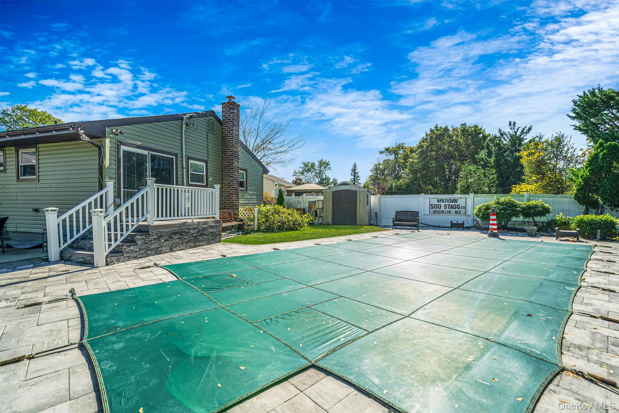 Backyard featuring a paved stone patio, in-ground swimming pool with safety cover, brick chimney, white vinyl perimeter fencing, and an exterior storage structure Backyard featuring a paved stone patio, in-ground swimming pool with safety cover, brick chimney, white vinyl perimeter fencing, and an exterior storage structure