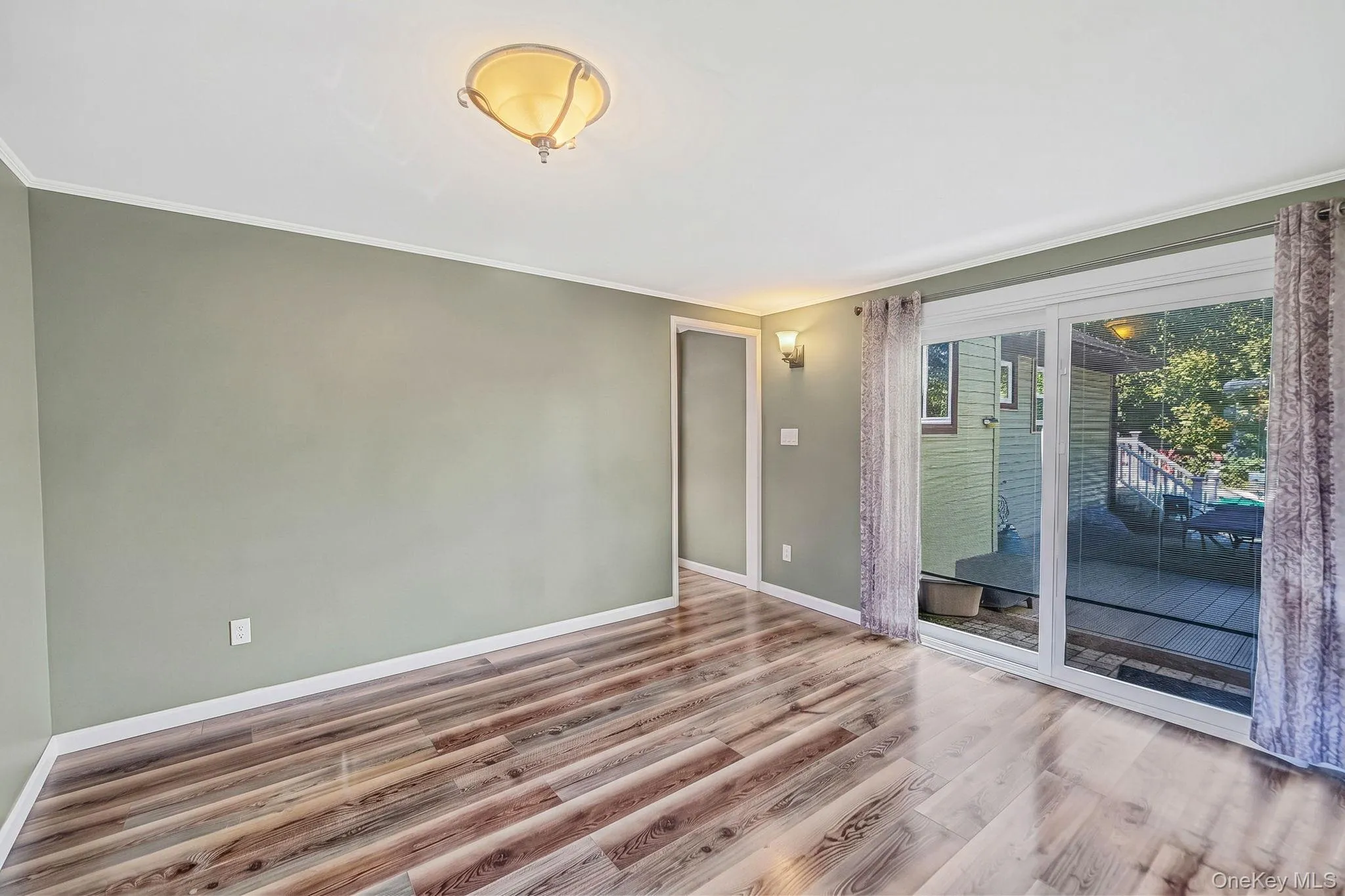 Interior space featuring wood-finish flooring, a semi-flush mount ceiling fixture, wall-mounted accent lighting, and a sliding glass door Interior space featuring wood-finish flooring, a semi-flush mount ceiling fixture, wall-mounted accent lighting, and a sliding glass door