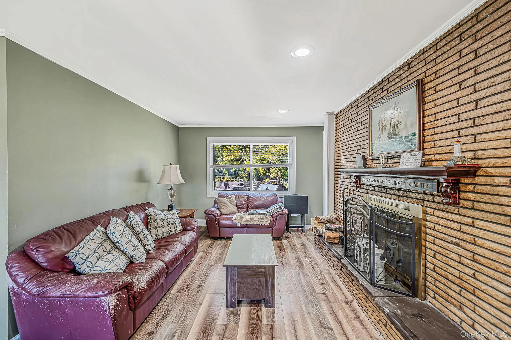 Living area featuring wood-finish flooring, recessed lighting, and a floor-to-ceiling brick fireplace with a decorative wooden mantel and raised stone hearth Living area featuring wood-finish flooring, recessed lighting, and a floor-to-ceiling brick fireplace with a decorative wooden mantel and raised stone hearth