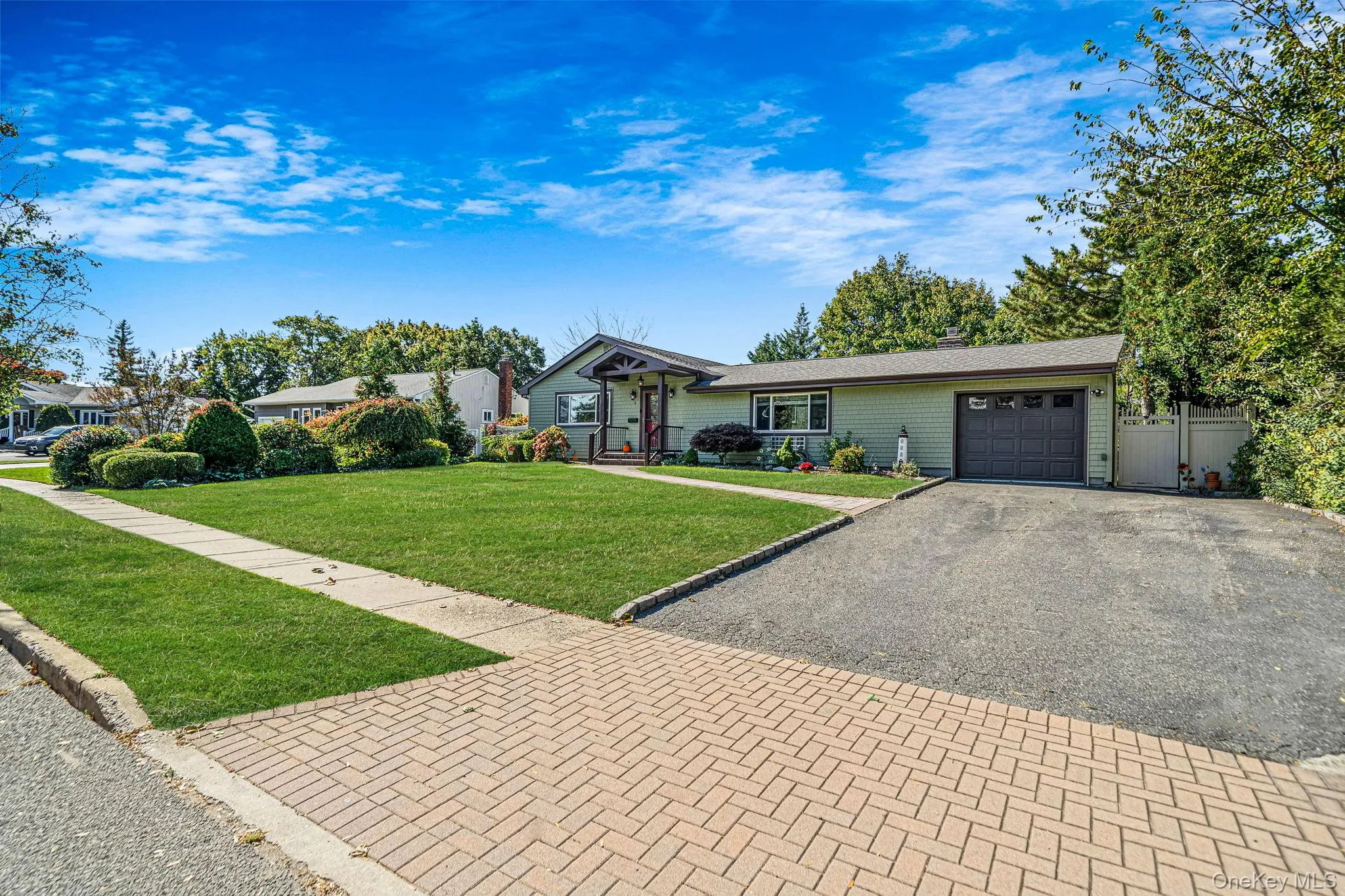 Single-story residence featuring horizontal siding, a covered front entryway, attached one-car garage, herringbone-patterned paved driveway, and established landscaping Single-story residence featuring horizontal siding, a covered front entryway, attached one-car garage, herringbone-patterned paved driveway, and established landscaping