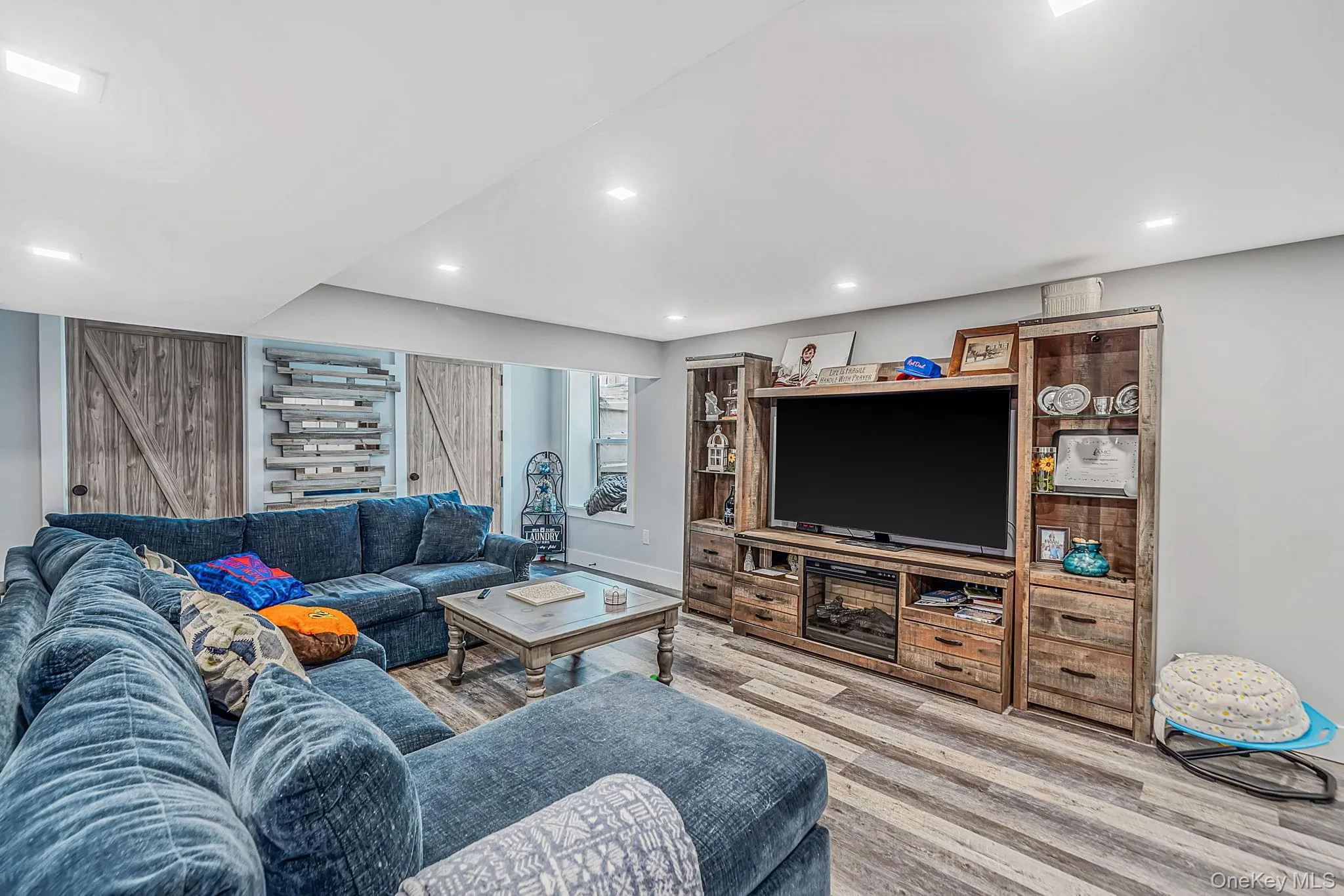 Recessed lighting, wood-finish flooring, built-in wooden media cabinetry with integrated electric fireplace, and wooden barn-style closet doors Recessed lighting, wood-finish flooring, built-in wooden media cabinetry with integrated electric fireplace, and wooden barn-style closet doors