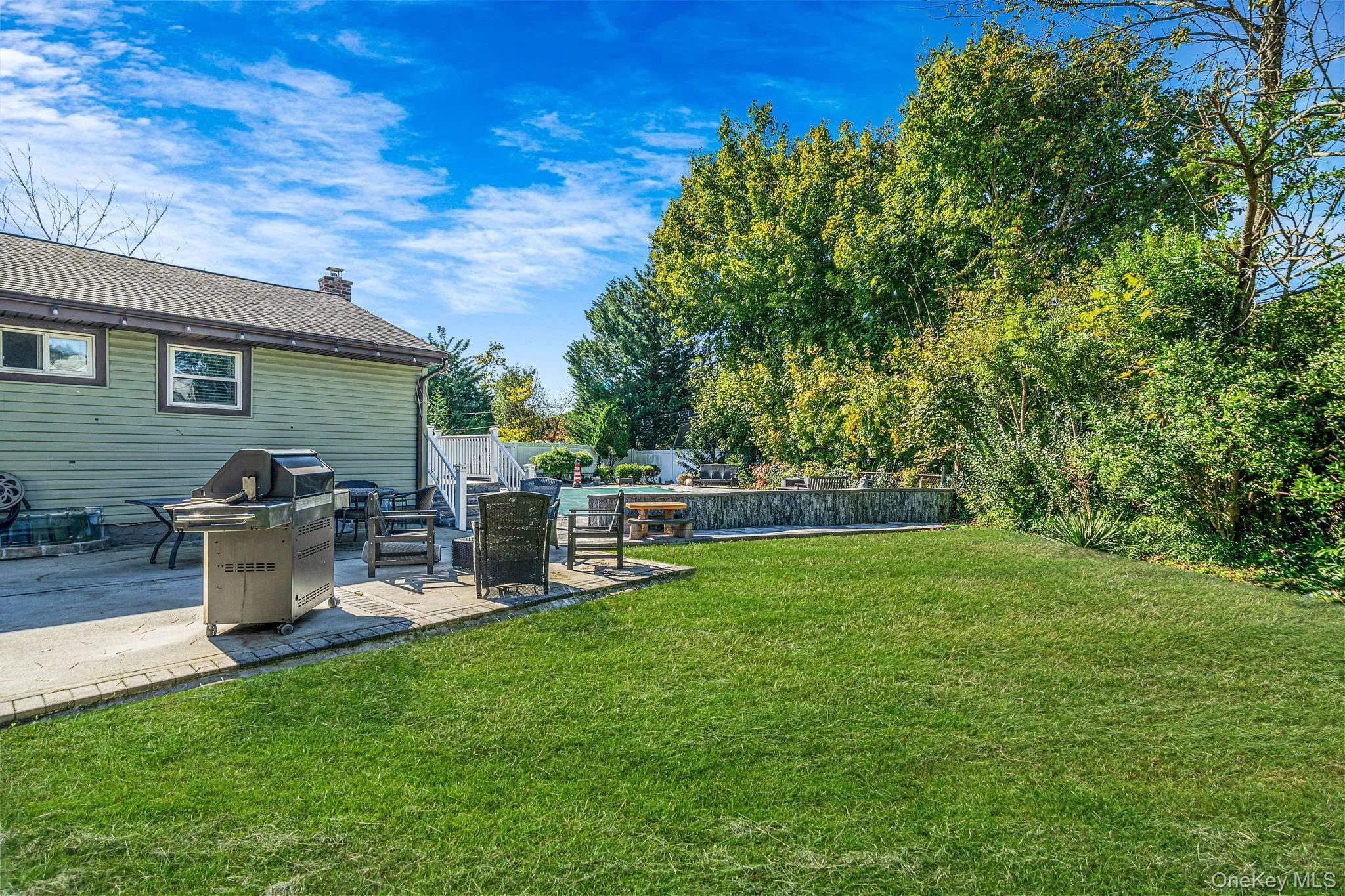 Backyard featuring a concrete patio, stone retaining wall, inground pool, and manicured lawn Backyard featuring a concrete patio, stone retaining wall, inground pool, and manicured lawn