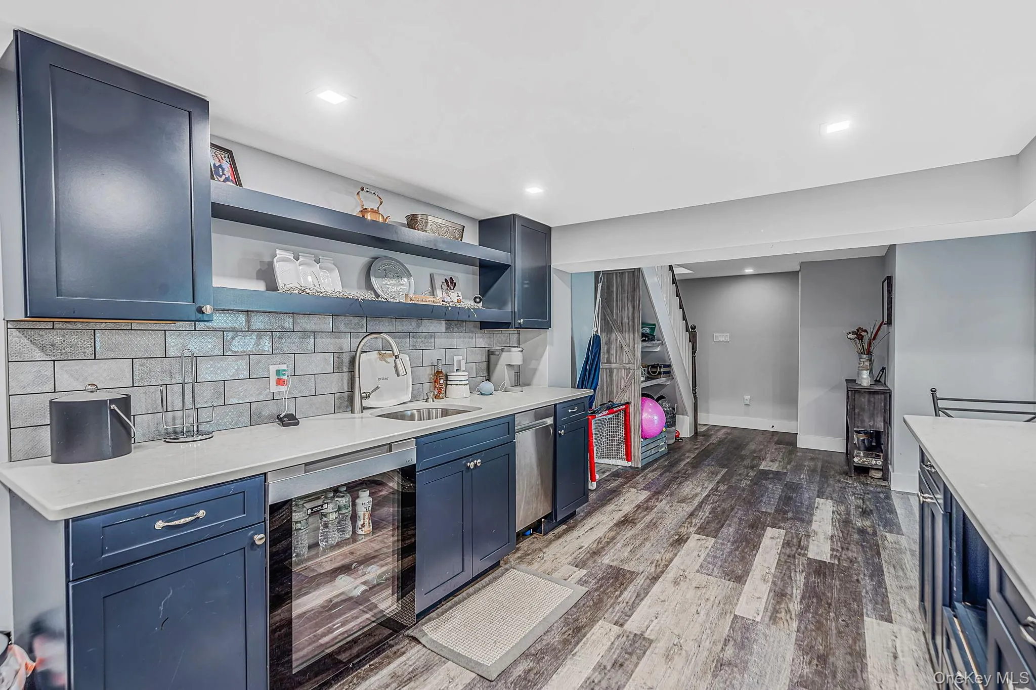 Dark navy cabinetry, subway tile backsplash, light-toned countertops, stainless steel undermount sink, and wood-finish flooring Dark navy cabinetry, subway tile backsplash, light-toned countertops, stainless steel undermount sink, and wood-finish flooring