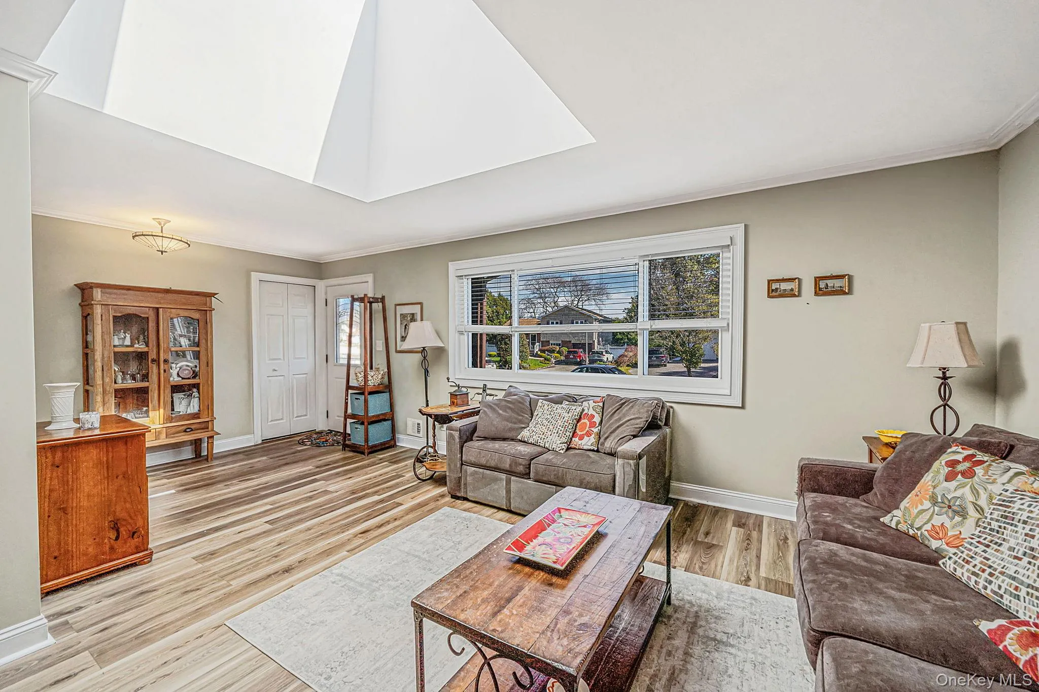 Living area featuring wood-finish flooring, a vaulted ceiling with a skylight, and a large horizontal window Living area featuring wood-finish flooring, a vaulted ceiling with a skylight, and a large horizontal window
