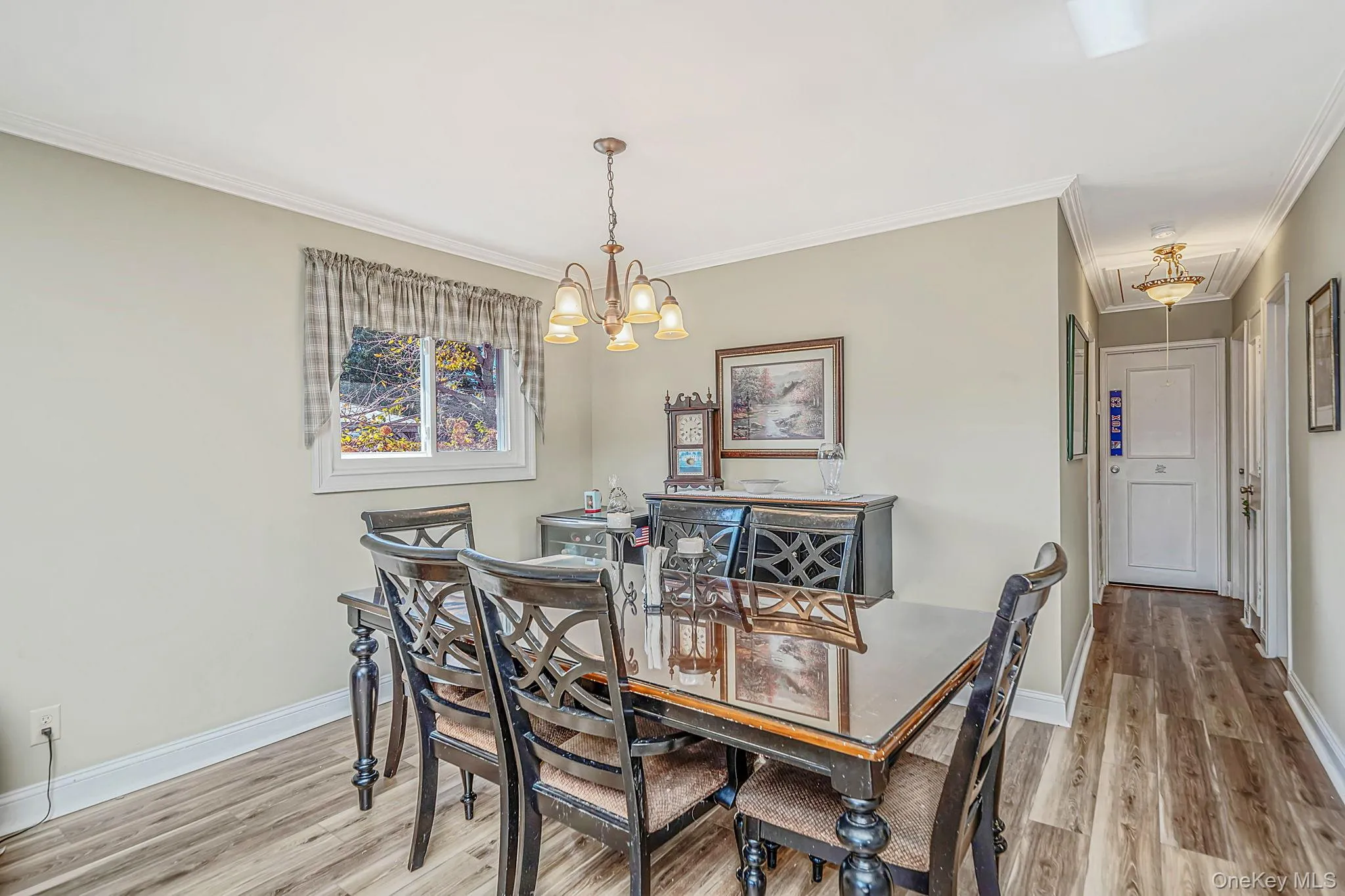 Dining area featuring wood-finish flooring, a multi-arm chandelier, crown molding, and a single-pane window Dining area featuring wood-finish flooring, a multi-arm chandelier, crown molding, and a single-pane window