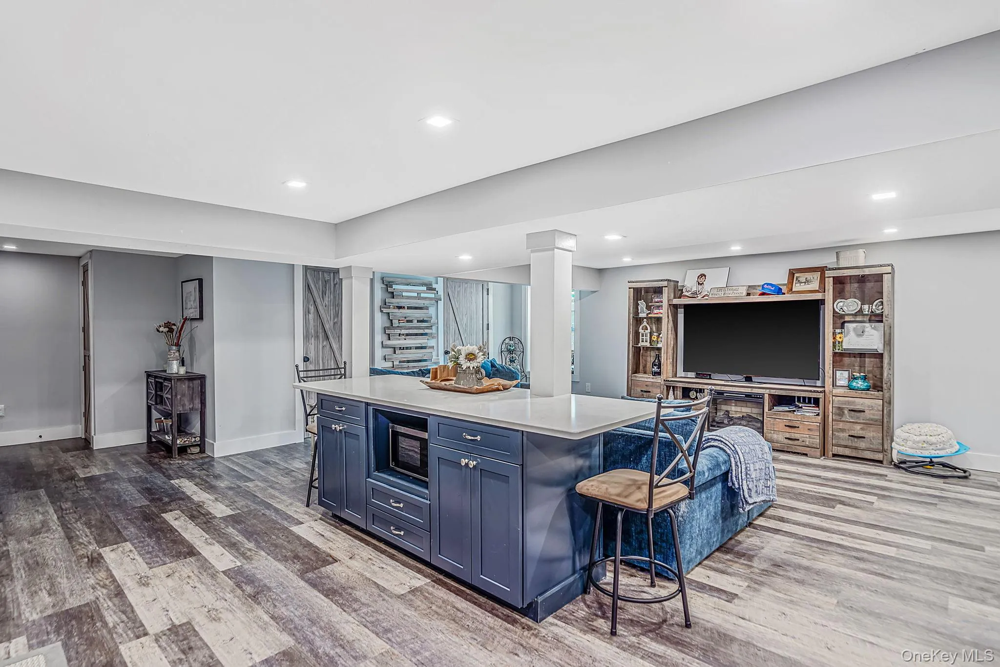 Large central island featuring navy cabinetry, a light-toned countertop, and integrated microwave, complemented by wood-finish flooring and recessed lighting Large central island featuring navy cabinetry, a light-toned countertop, and integrated microwave, complemented by wood-finish flooring and recessed lighting