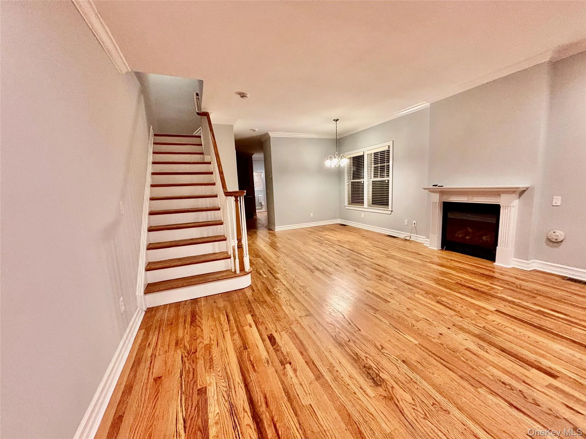 Unfurnished living room with a fireplace, a chandelier, stairs, light wood-type flooring, and crown molding Unfurnished living room with a fireplace, a chandelier, stairs, light wood-type flooring, and crown molding