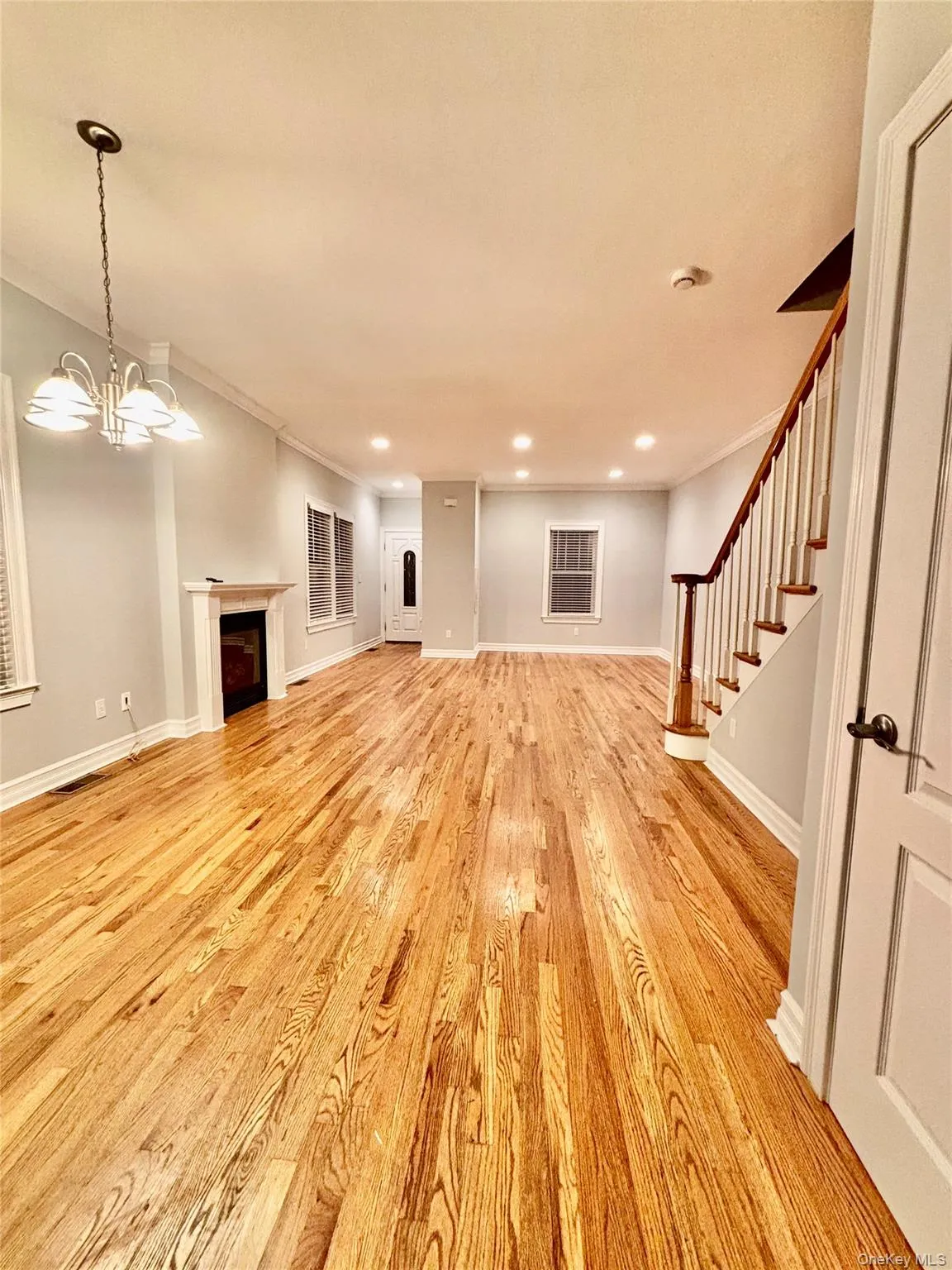Unfurnished living room featuring a fireplace, stairway, light wood finished floors, a chandelier, and crown molding Unfurnished living room featuring a fireplace, stairway, light wood finished floors, a chandelier, and crown molding