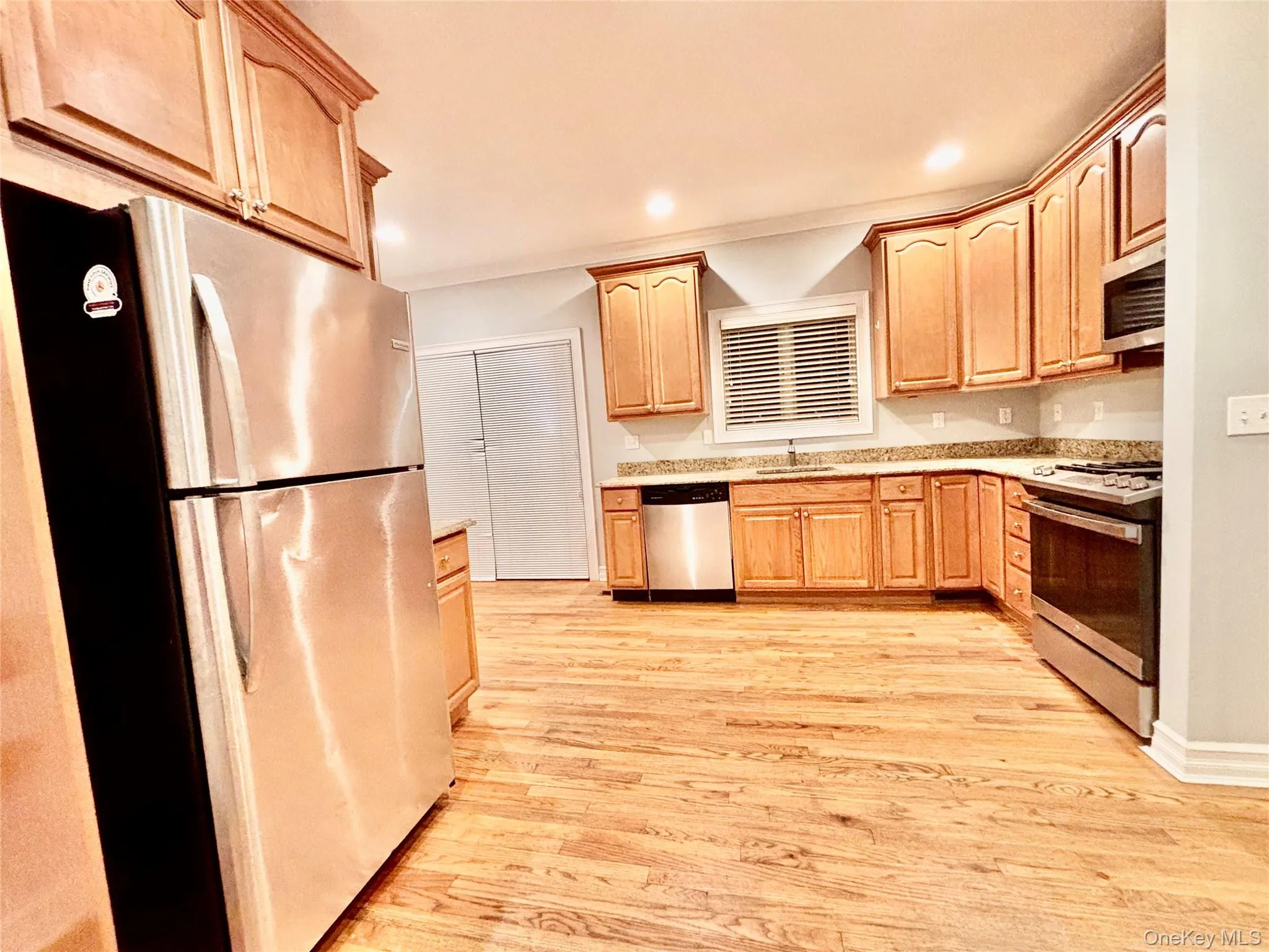 Kitchen featuring appliances with stainless steel finishes, light brown cabinetry, light wood-type flooring, recessed lighting, and light stone countertops Kitchen featuring appliances with stainless steel finishes, light brown cabinetry, light wood-type flooring, recessed lighting, and light stone countertops