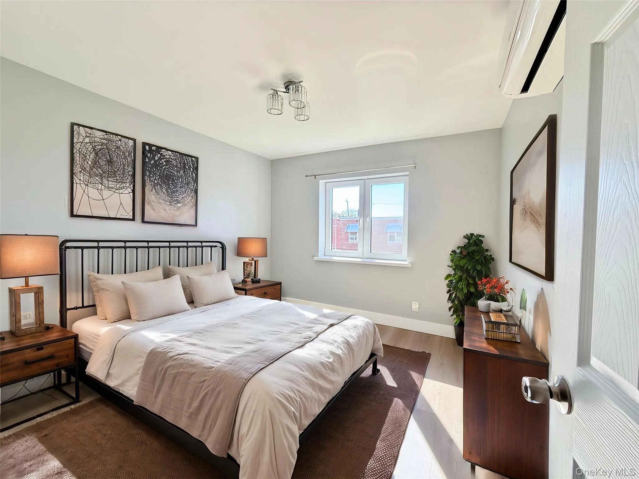 Room featuring light-toned walls, wood-finish flooring, a dual-pane window, and a wall-mounted ductless climate control unit Room featuring light-toned walls, wood-finish flooring, a dual-pane window, and a wall-mounted ductless climate control unit