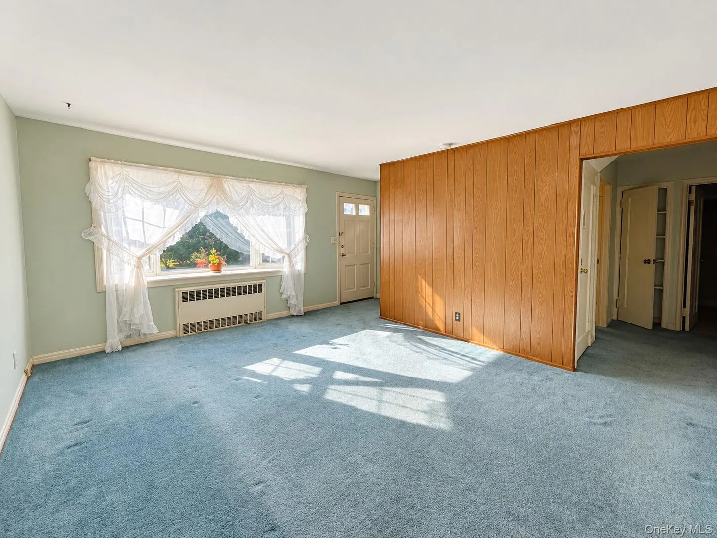 Living area featuring wood-paneled accent wall, neutral wall coloring, and wall-to-wall carpeting Living area featuring wood-paneled accent wall, neutral wall coloring, and wall-to-wall carpeting