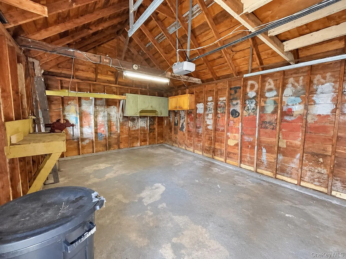 Detached garage featuring exposed wood framing, concrete flooring, built-in wall cabinetry, and an integrated workbench Detached garage featuring exposed wood framing, concrete flooring, built-in wall cabinetry, and an integrated workbench