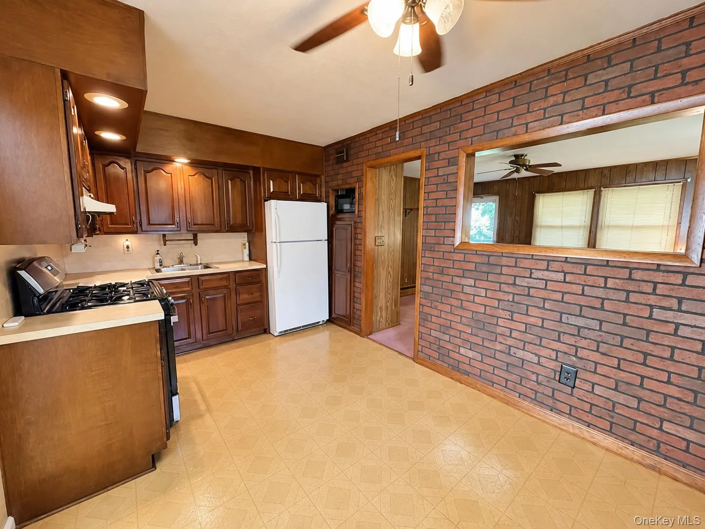 Kitchen featuring wood cabinetry, recessed lighting, a pass-through window with wooden trim, and an exposed brick accent wall Kitchen featuring wood cabinetry, recessed lighting, a pass-through window with wooden trim, and an exposed brick accent wall