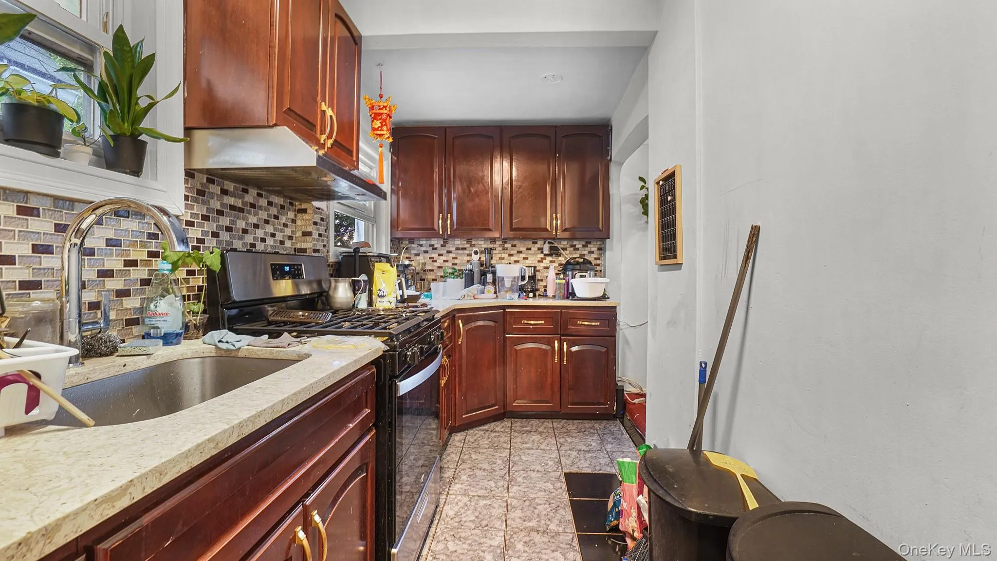 Kitchen featuring wood cabinetry, multicolor glass tile backsplash, stone-finish countertops, stainless steel sink with high-arc faucet, and ceramic tile flooring Kitchen featuring wood cabinetry, multicolor glass tile backsplash, stone-finish countertops, stainless steel sink with high-arc faucet, and ceramic tile flooring