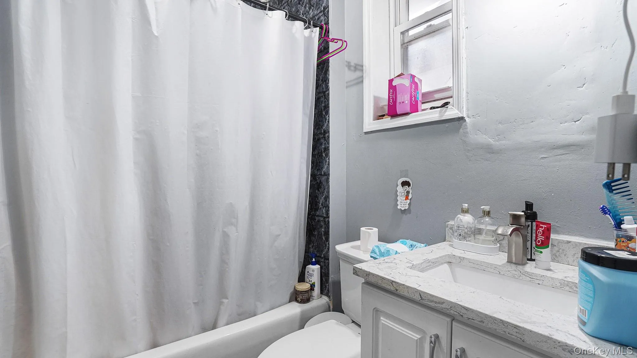 Bathroom featuring a stone-pattern vanity countertop, white cabinet storage, single-handle faucet, and tiled shower surround Bathroom featuring a stone-pattern vanity countertop, white cabinet storage, single-handle faucet, and tiled shower surround