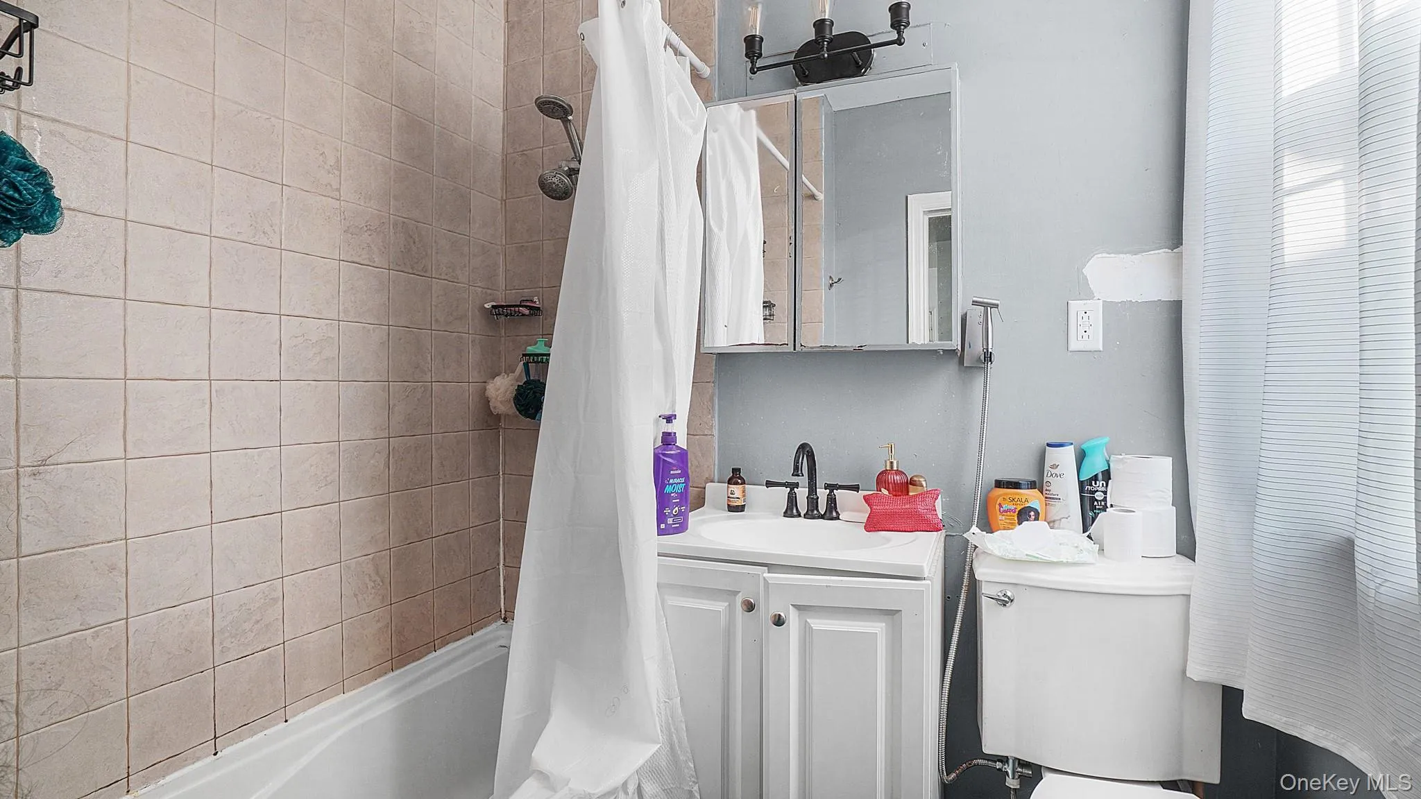Bathroom featuring square tile tub surround, white vanity cabinet with a curved sink, metal dual-handle faucet, and mirrored medicine cabinet Bathroom featuring square tile tub surround, white vanity cabinet with a curved sink, metal dual-handle faucet, and mirrored medicine cabinet