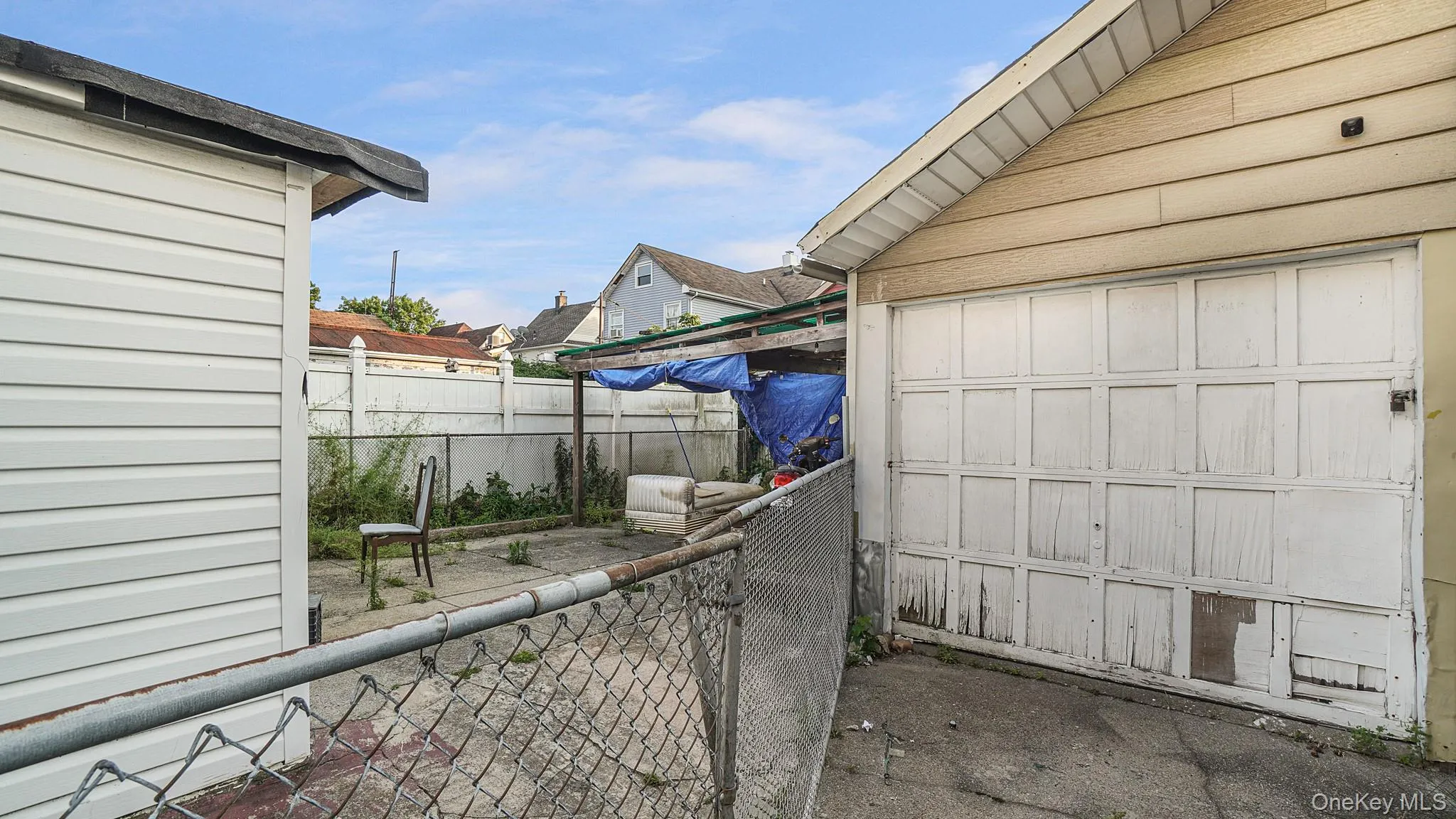 Exterior detached garage featuring horizontal siding and a multi-panel overhead door, accompanied by a paved area and enclosed fencing Exterior detached garage featuring horizontal siding and a multi-panel overhead door, accompanied by a paved area and enclosed fencing