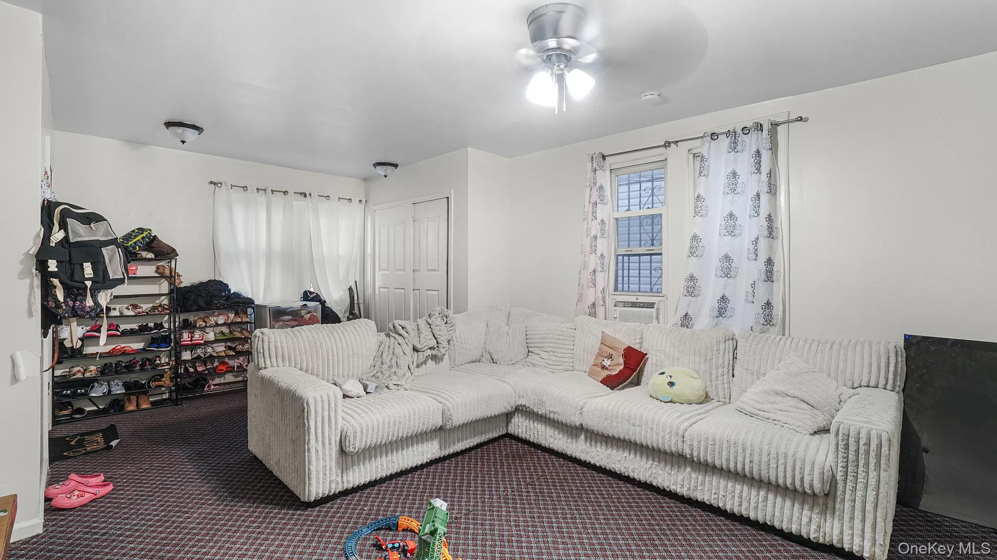 Interior room featuring wall-to-wall carpeting, a ceiling fan with integrated lighting, dual windows, and a built-in closet with double doors Interior room featuring wall-to-wall carpeting, a ceiling fan with integrated lighting, dual windows, and a built-in closet with double doors