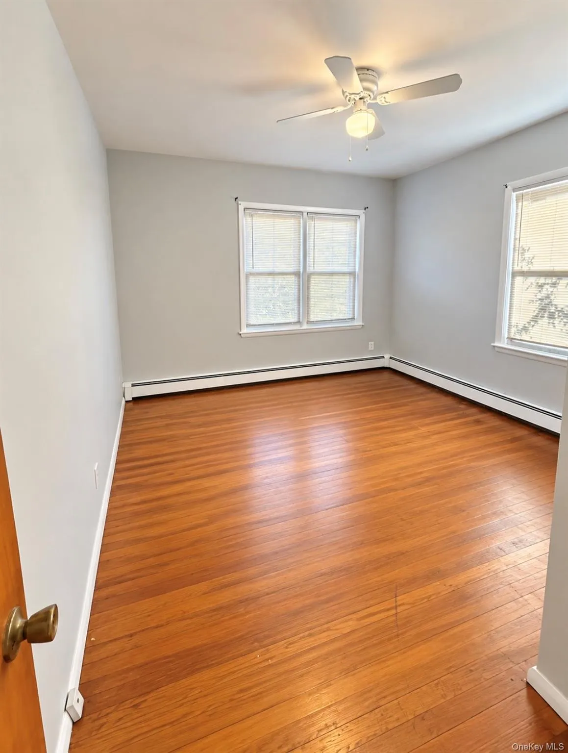 Wood-finish flooring, dual windows with blinds, and a white ceiling fan with integrated lighting Wood-finish flooring, dual windows with blinds, and a white ceiling fan with integrated lighting