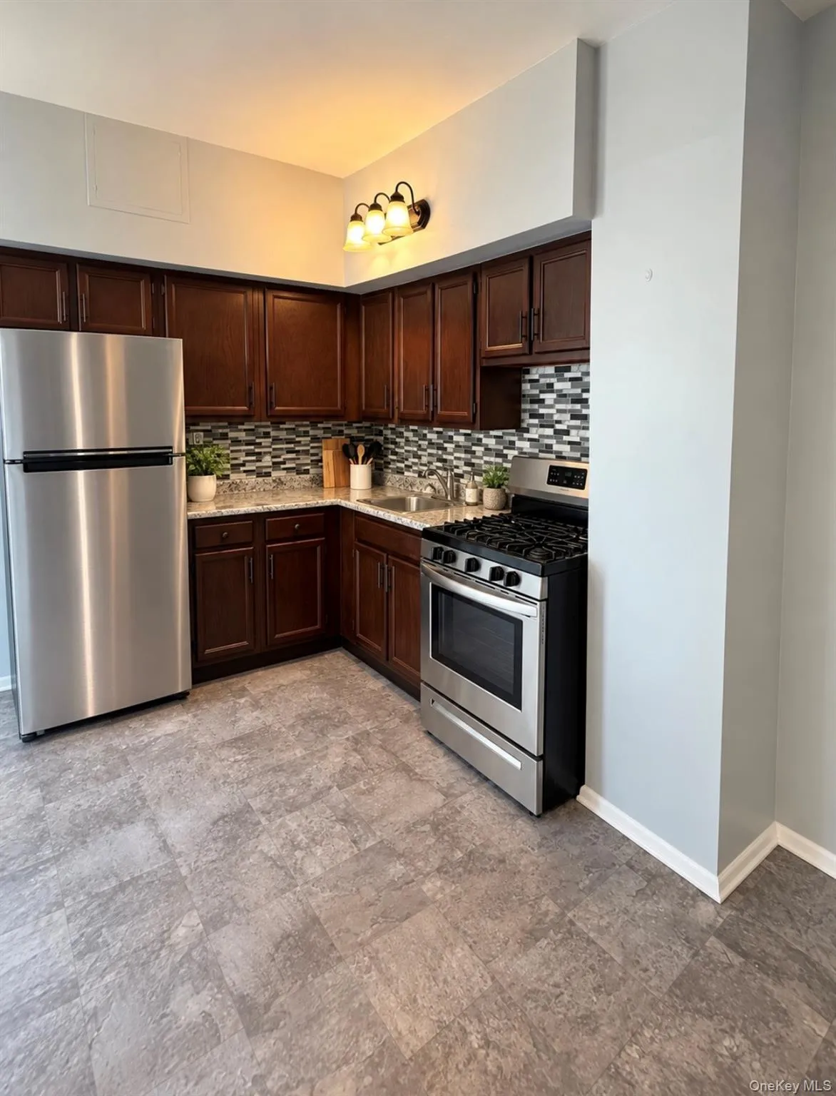 Kitchen featuring dark wood cabinetry, stainless steel appliances, multi-tonal mosaic tile backsplash, and light-toned stone-finish countertops Kitchen featuring dark wood cabinetry, stainless steel appliances, multi-tonal mosaic tile backsplash, and light-toned stone-finish countertops