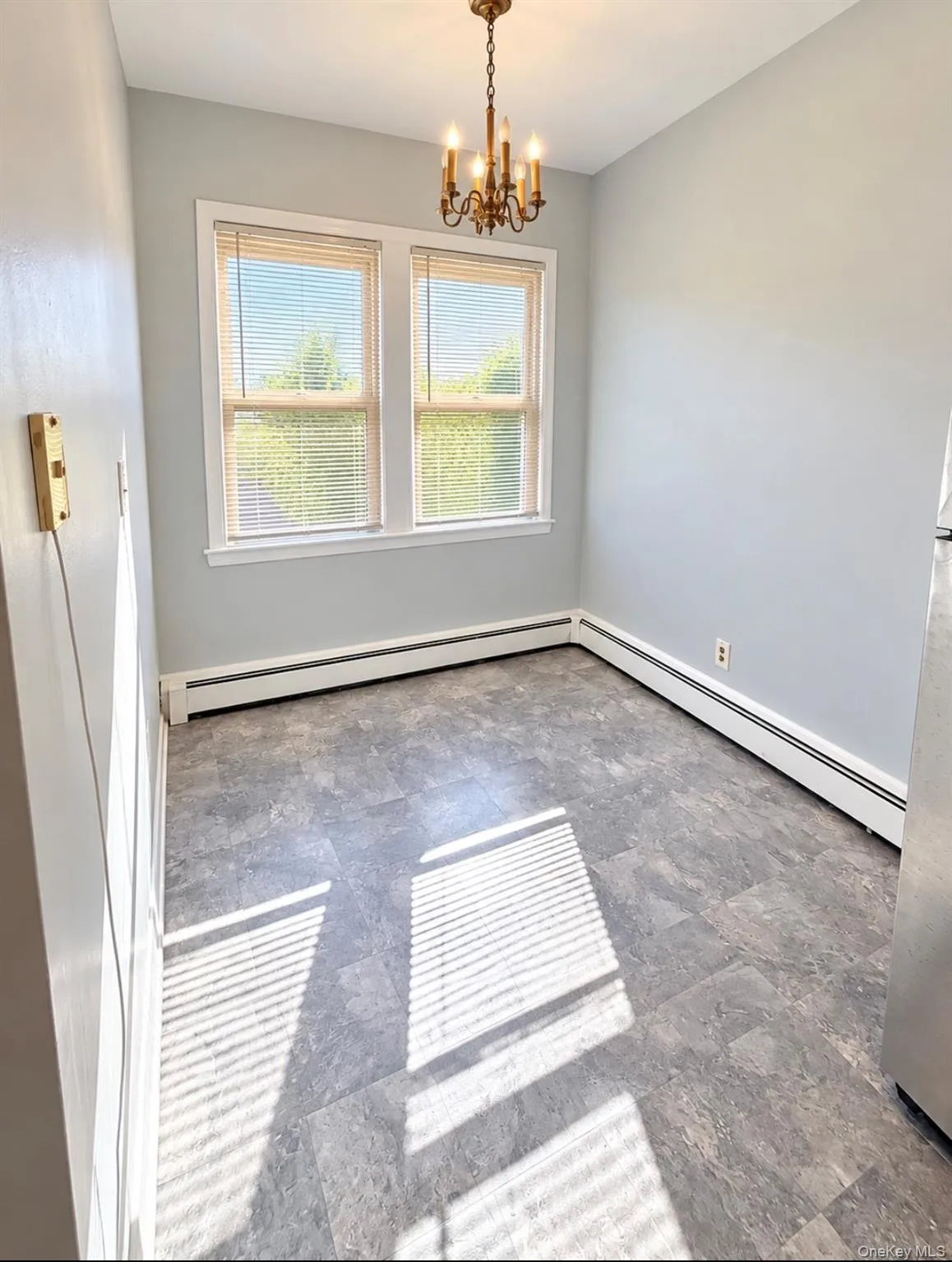 Room featuring dual-pane windows, a classic metal chandelier, and stone-finish flooring Room featuring dual-pane windows, a classic metal chandelier, and stone-finish flooring