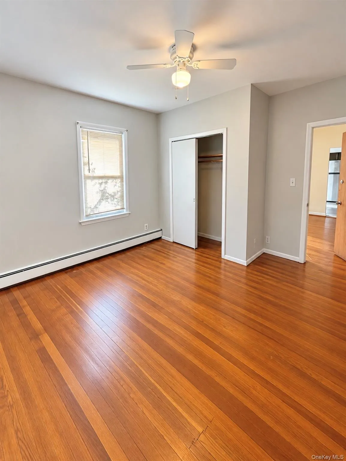 Wood-finish flooring, neutral wall tones, white-framed window, and overhead ceiling fan with light fixture Wood-finish flooring, neutral wall tones, white-framed window, and overhead ceiling fan with light fixture
