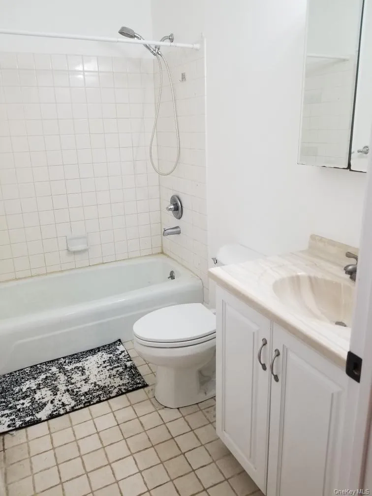 Bathroom featuring a white vanity with a neutral stone-finish countertop, an integrated sink, a porcelain tub with a tiled surround, and a wall-mounted medicine cabinet Bathroom featuring a white vanity with a neutral stone-finish countertop, an integrated sink, a porcelain tub with a tiled surround, and a wall-mounted medicine cabinet