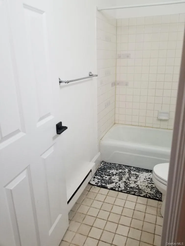 Bathroom featuring a white panel door with matte black hardware, square ceramic floor tiling, a porcelain tub with tile surround, and a metallic towel bar Bathroom featuring a white panel door with matte black hardware, square ceramic floor tiling, a porcelain tub with tile surround, and a metallic towel bar