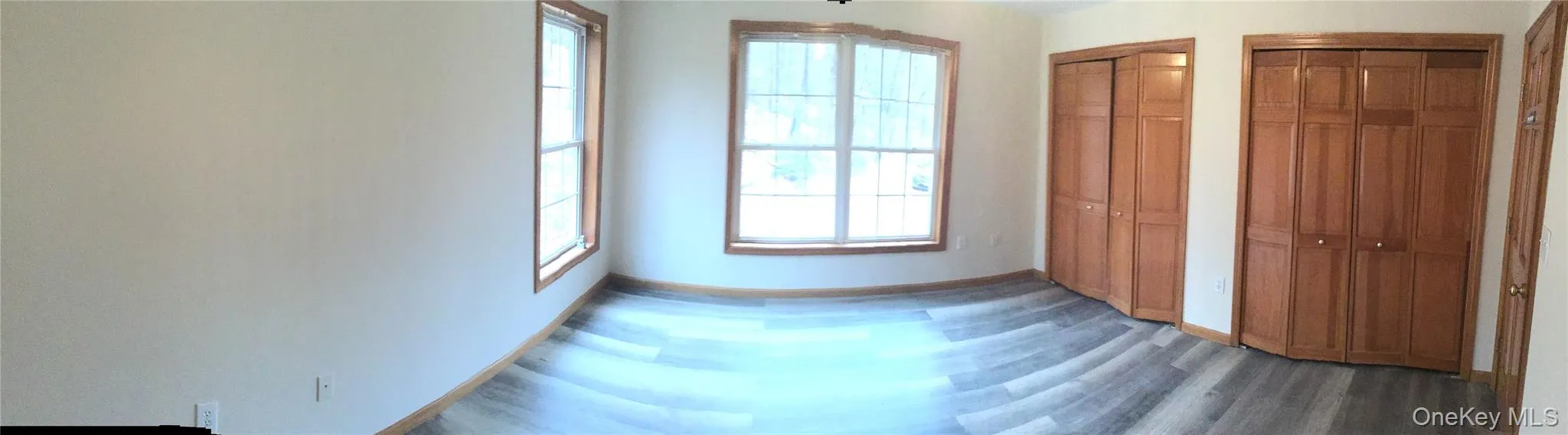 Unfurnished bedroom featuring two closets, multiple windows, and wood finished floors Unfurnished bedroom featuring two closets, multiple windows, and wood finished floors