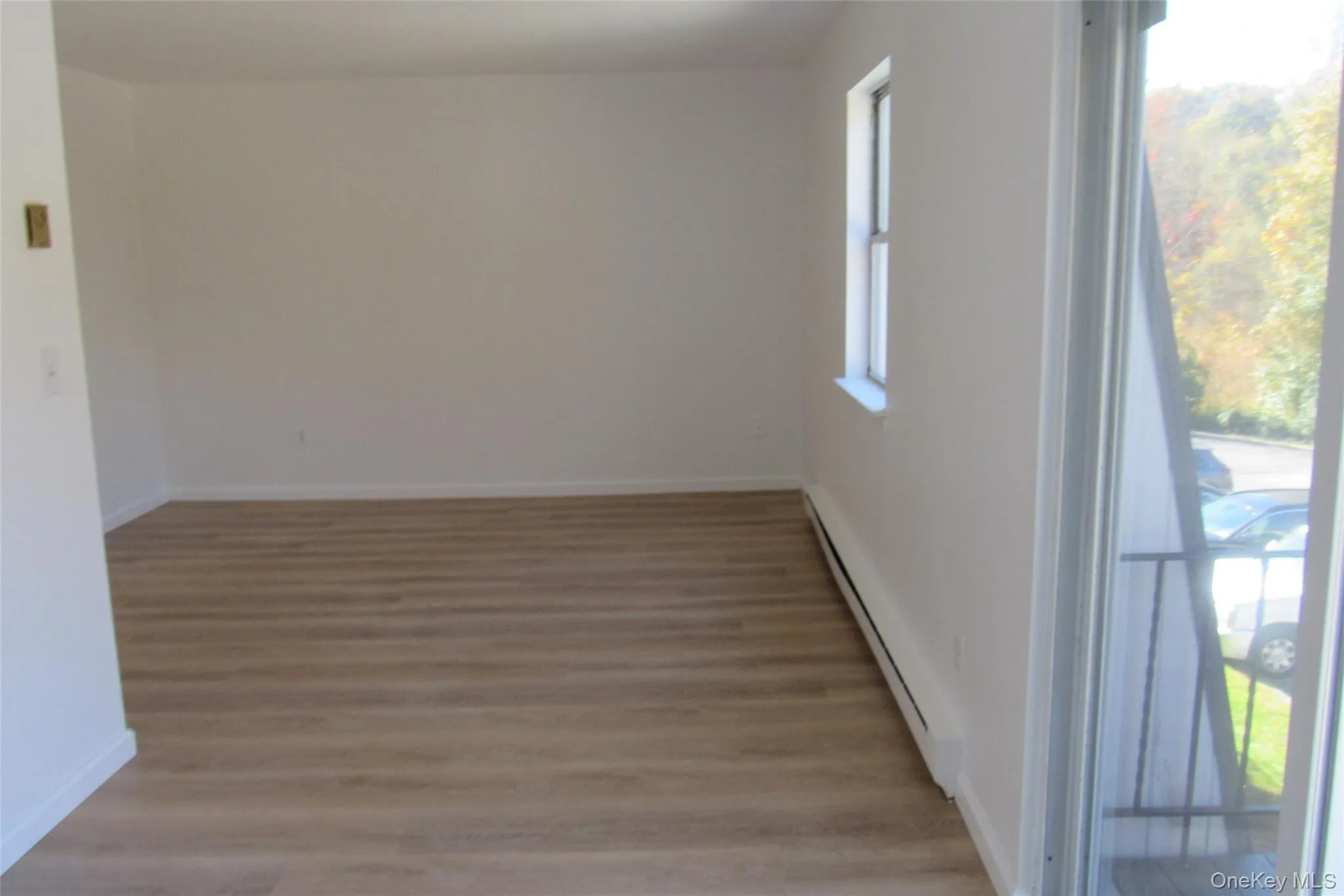 Interior space featuring wood-finish flooring, white walls, and a glass sliding door providing balcony access Interior space featuring wood-finish flooring, white walls, and a glass sliding door providing balcony access