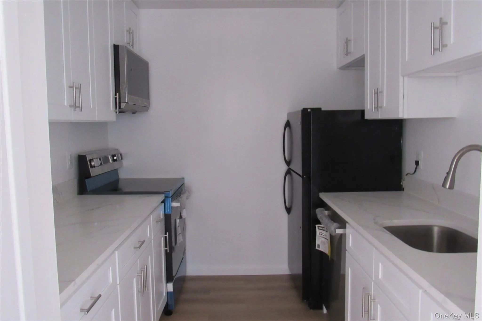 Kitchen featuring white shaker-style cabinetry, quart surface countertops, wood-finish flooring, stainless steel sink with high-arc faucet, and new black kitchen appliances Kitchen featuring white shaker-style cabinetry, quart surface countertops, wood-finish flooring, stainless steel sink with high-arc faucet, and new black kitchen appliances