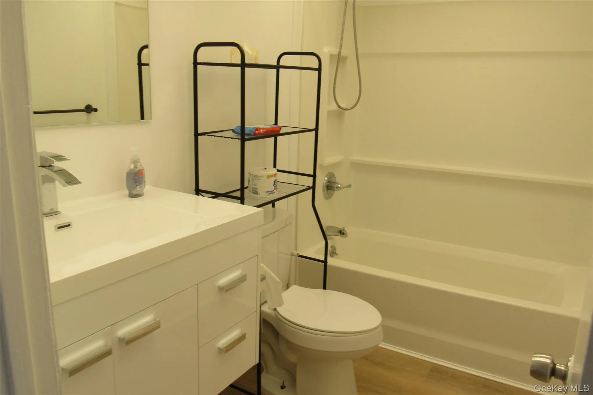 Bathroom featuring a white vanity cabinet, rectangular undermount sink, chrome faucet, and a tub-shower combination with integrated shelving Bathroom featuring a white vanity cabinet, rectangular undermount sink, chrome faucet, and a tub-shower combination with integrated shelving