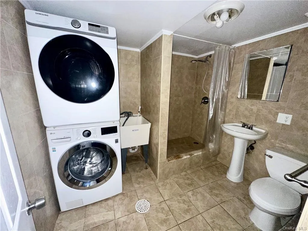 Lower Level - Full bathroom with Clothes washing area and slop sink, with ornamental molding, sink, tile walls, and stacked washer / drying machine Lower Level - Full bathroom with Clothes washing area and slop sink, with ornamental molding, sink, tile walls, and stacked washer / drying machine
