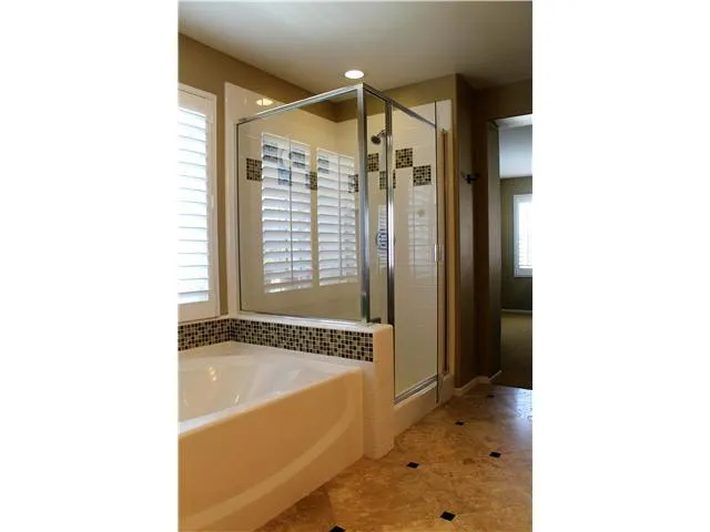 The travertine floors, glass tile, and plantation shutters contribute to the clean finished look of the master bath