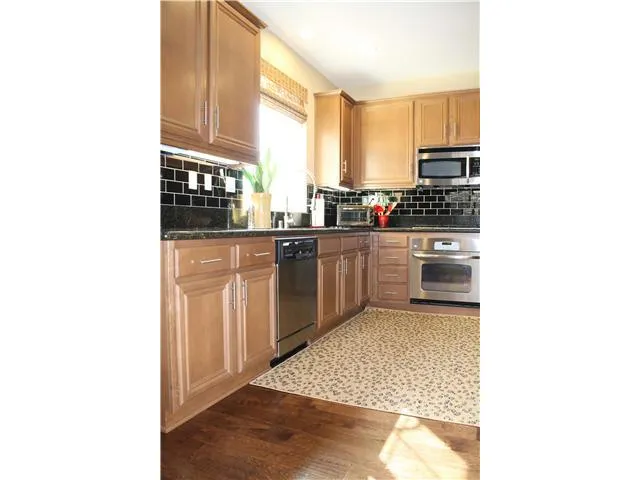Maple wood flooring continues into kitchen with subway tile backsplash from counter to underside of upper cabinets