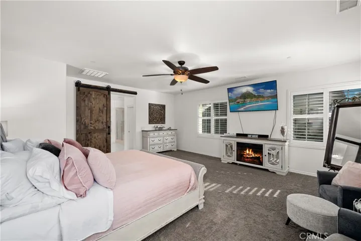 Primary suite is your own private oasis, as it is oversized and allows for your couch area, bed, and several extra pieces of furniture!  Barn door is modern and pulls all of the wood tones nicely together, and allows you to seperate the en-suite from the bedroom when closed! Ceiling fan above. Several dual paned plantation shutter covered windows allows you to see the surrounding mountains and pool area accross the street!
