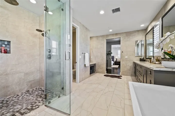 Master bathroom with double sinks, tile covered walls, vanity, freestanding soaking tub, and frameless glass shower.