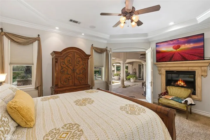 Primary suite with fireplace, ceiling fan, coffered ceiling, crown molding, walk-in closet and direct access to pool area
