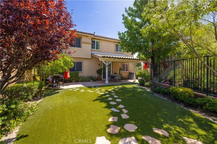 Backyard view of home with covered patio, fruit trees and drought resistant grass