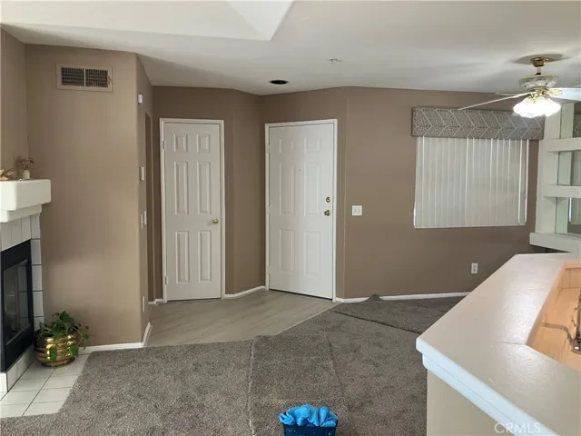 View of entryway to living room area, corner fireplace, utility closet, ceiling fan in eating area, kitchen counter new carpet throughout living area and bedrooms.