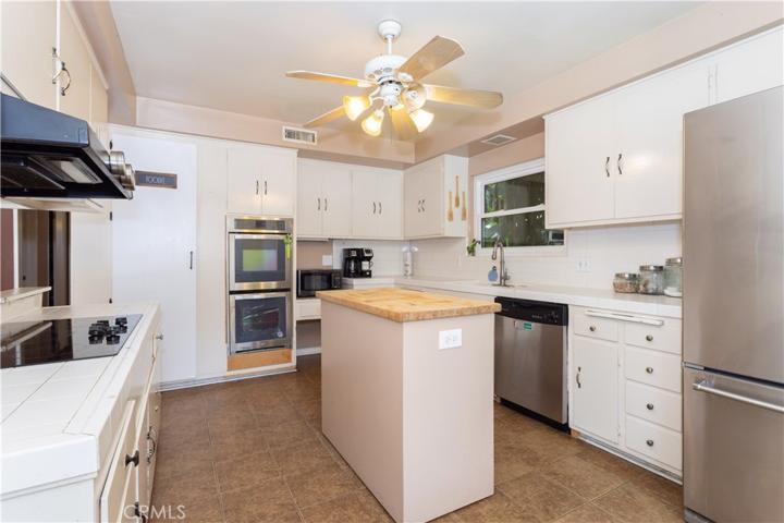 Kitchen with tiled counters, electric appliances and island.