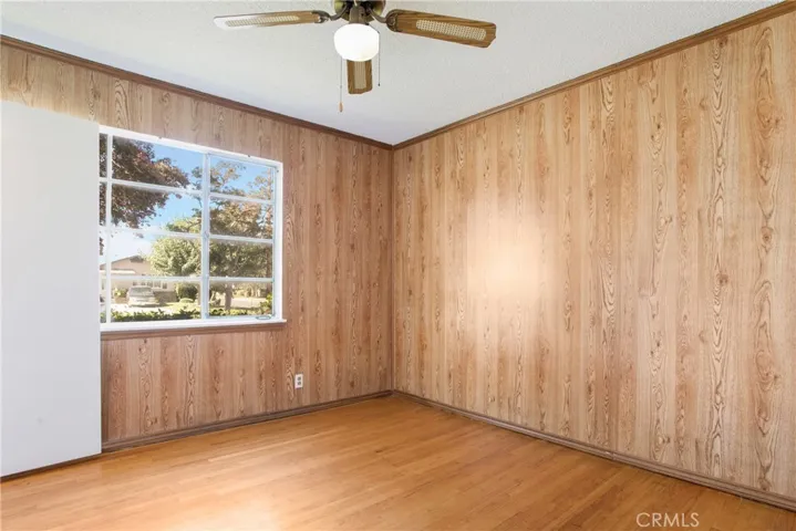 Middle bedroom has a large window, ceiling fan and wood paneling.