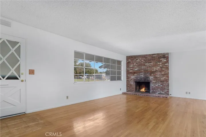 Large front room with red brick fireplace, wood mantle and large window offering lots of natural light