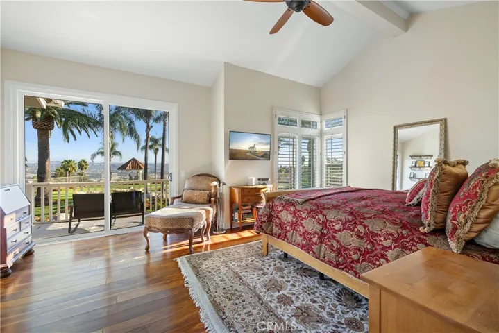 Primary bedroom with vaulted ceilings, ceiling fan, and a sliding door to the balcony.