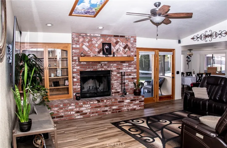 Living room with wood grain tile floors, vaulted ceiling, ceiling fan, brick faced fireplace, and access to rear yard.